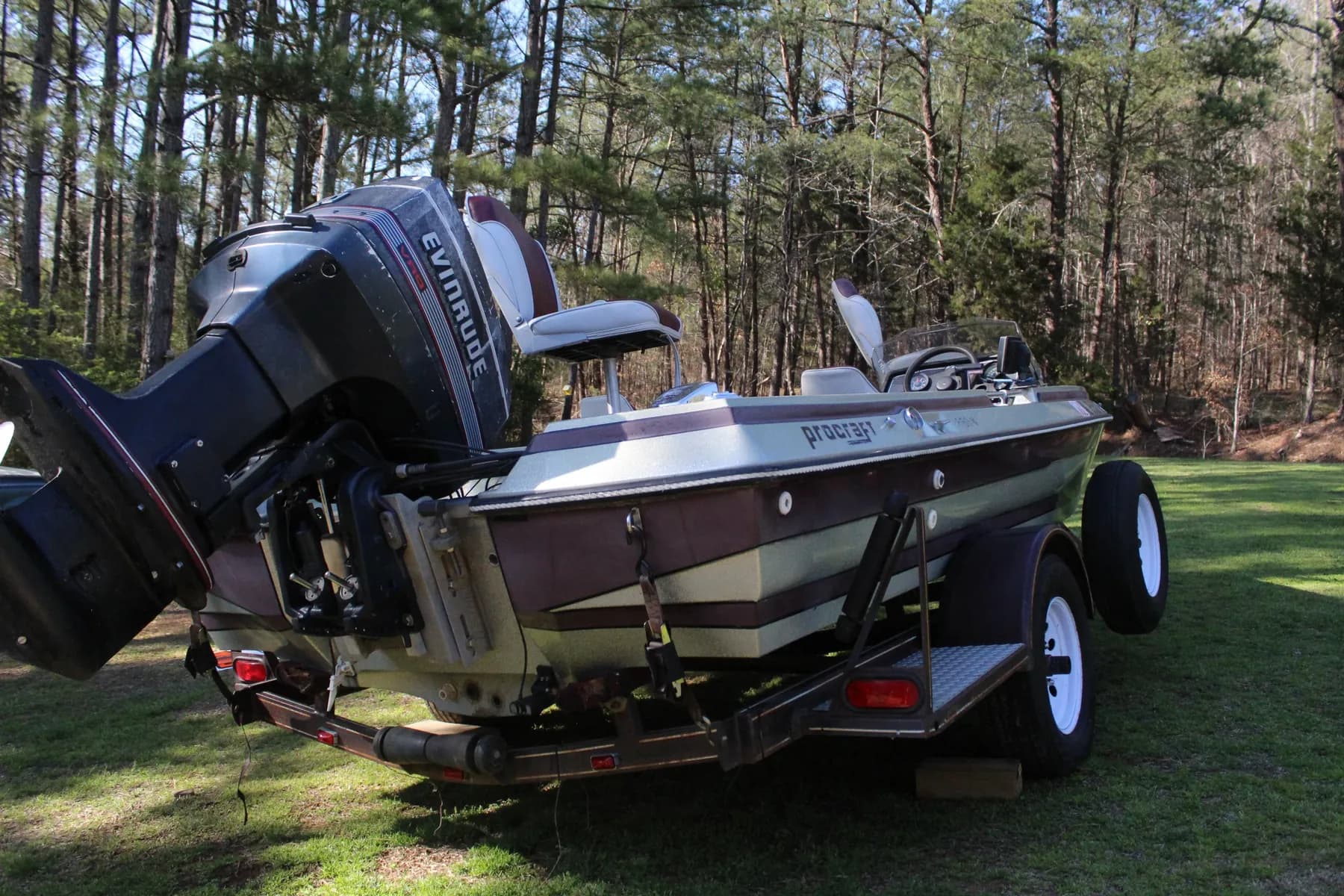 Bass boat with an Evinrude outboard on a trailer in a grassy clearing
