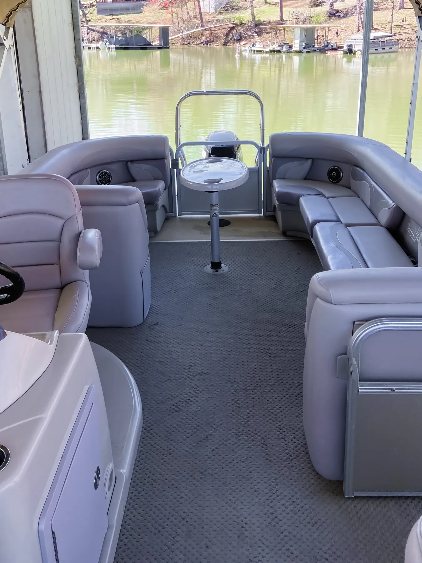 Gray lounge seating, table, and carpet on a pontoon boat in a covered slip