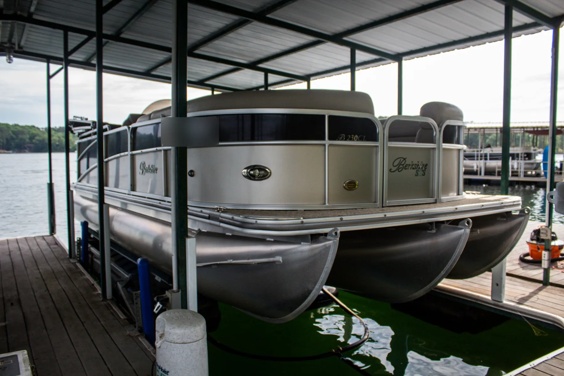 Silver pontoon boat raised on a lift under a covered dock