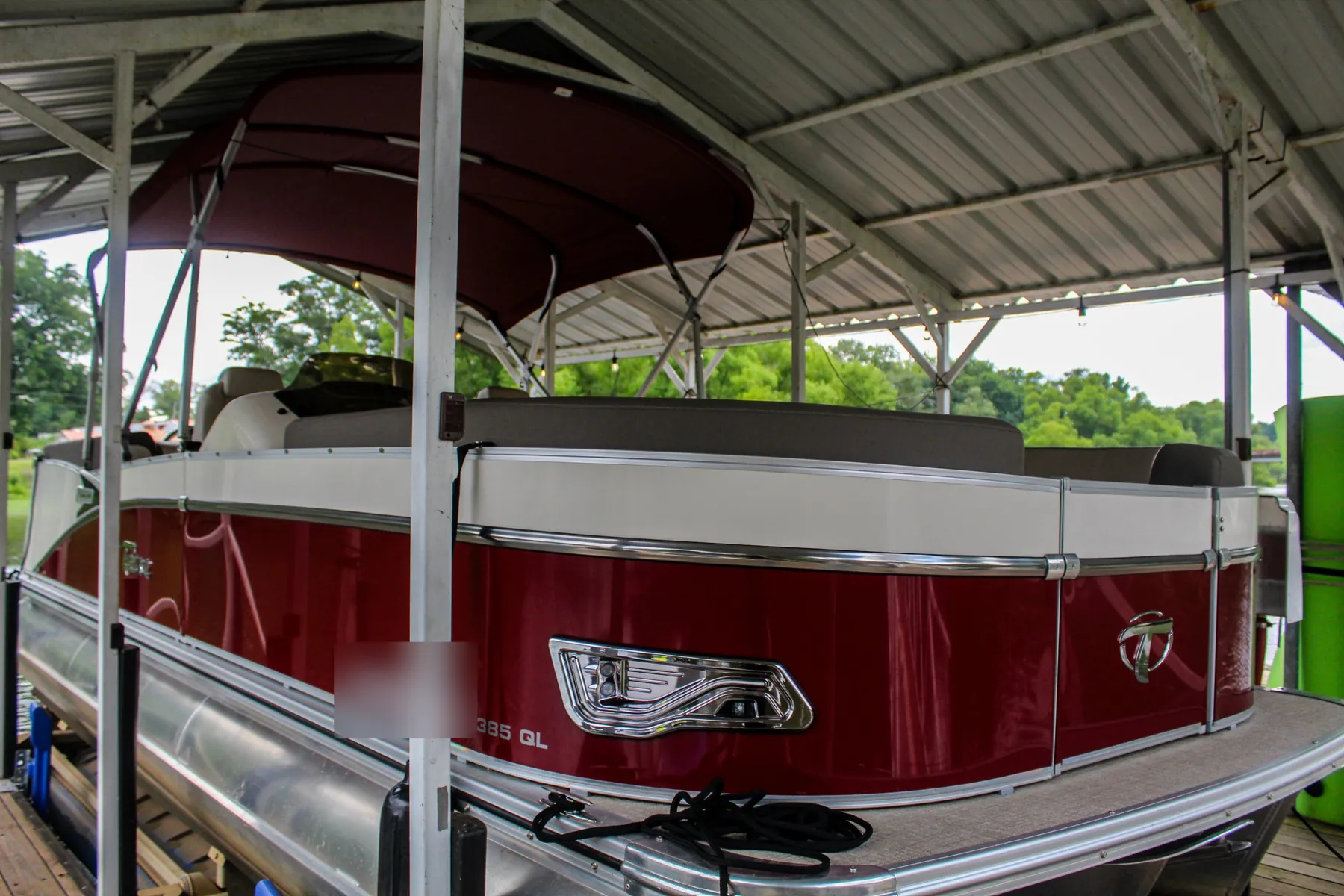 Red and white pontoon with a burgundy bimini top under a covered dock