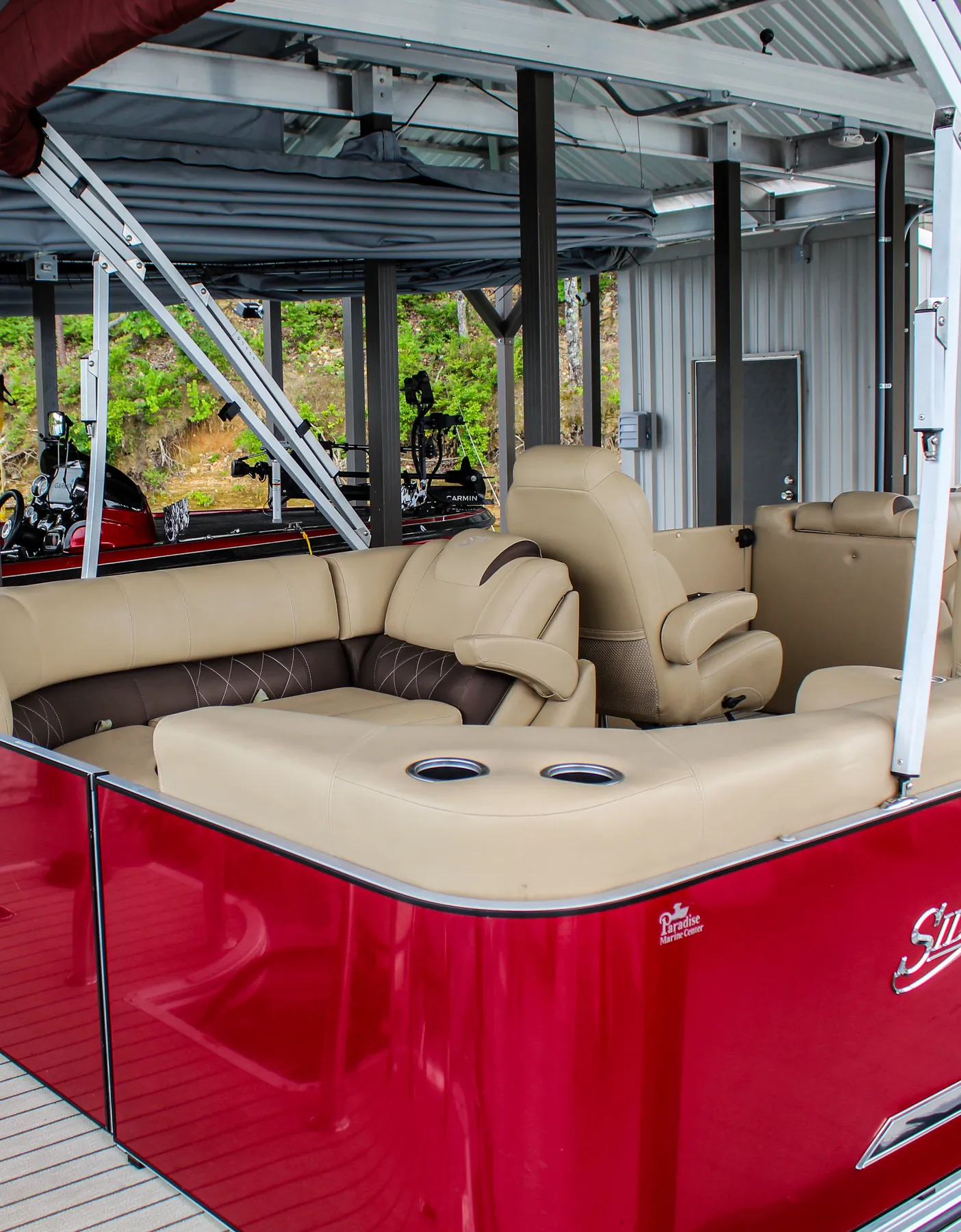 Red pontoon with tan lounge seating and a bimini top in a covered boat slip