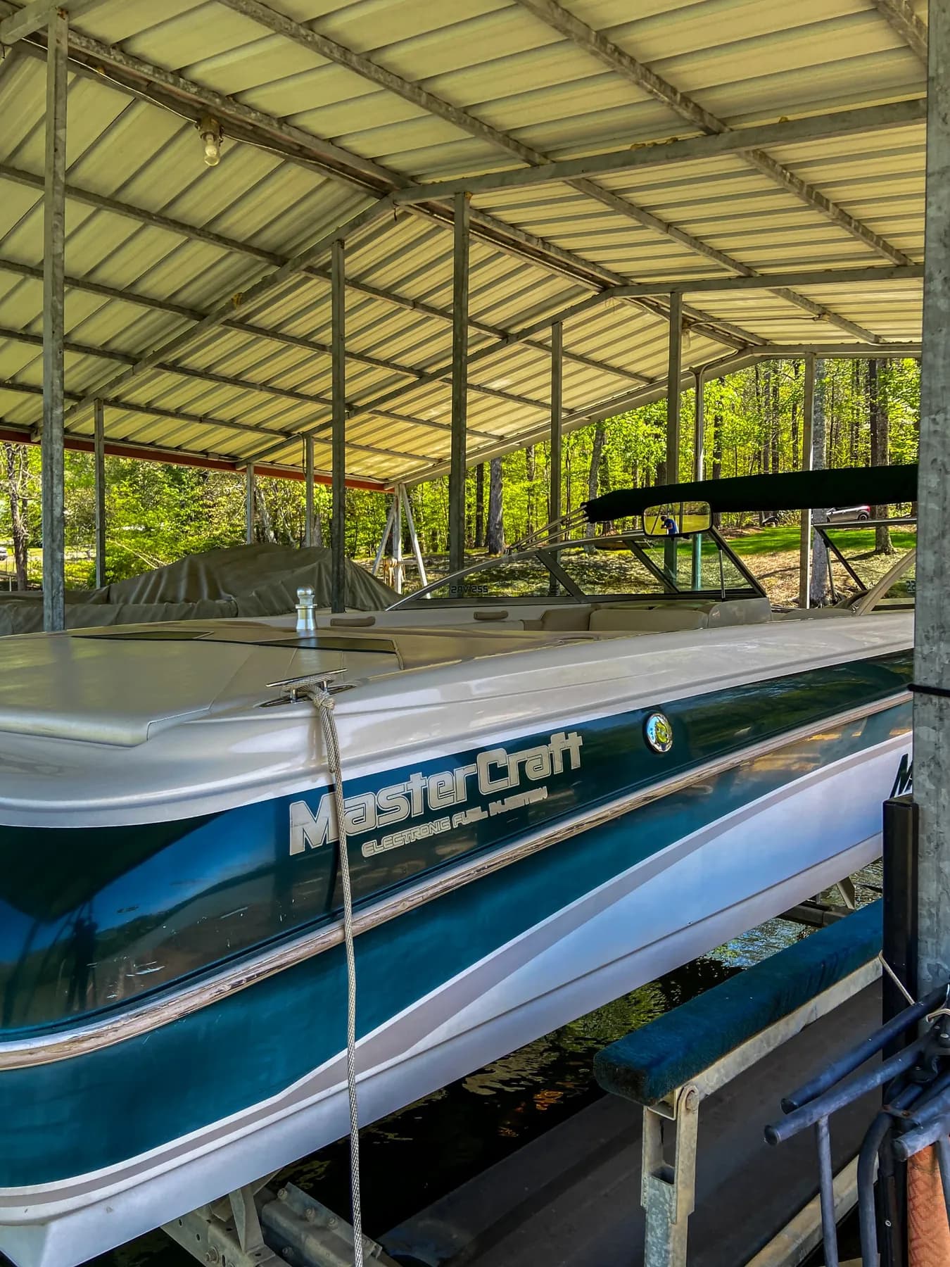 Teal and white ski boat on a lift inside a covered boat house