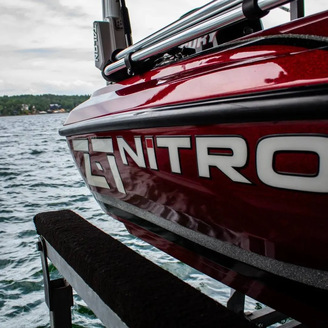 Close-up of a glossy red bass boat hull on a lift with the lake behind it