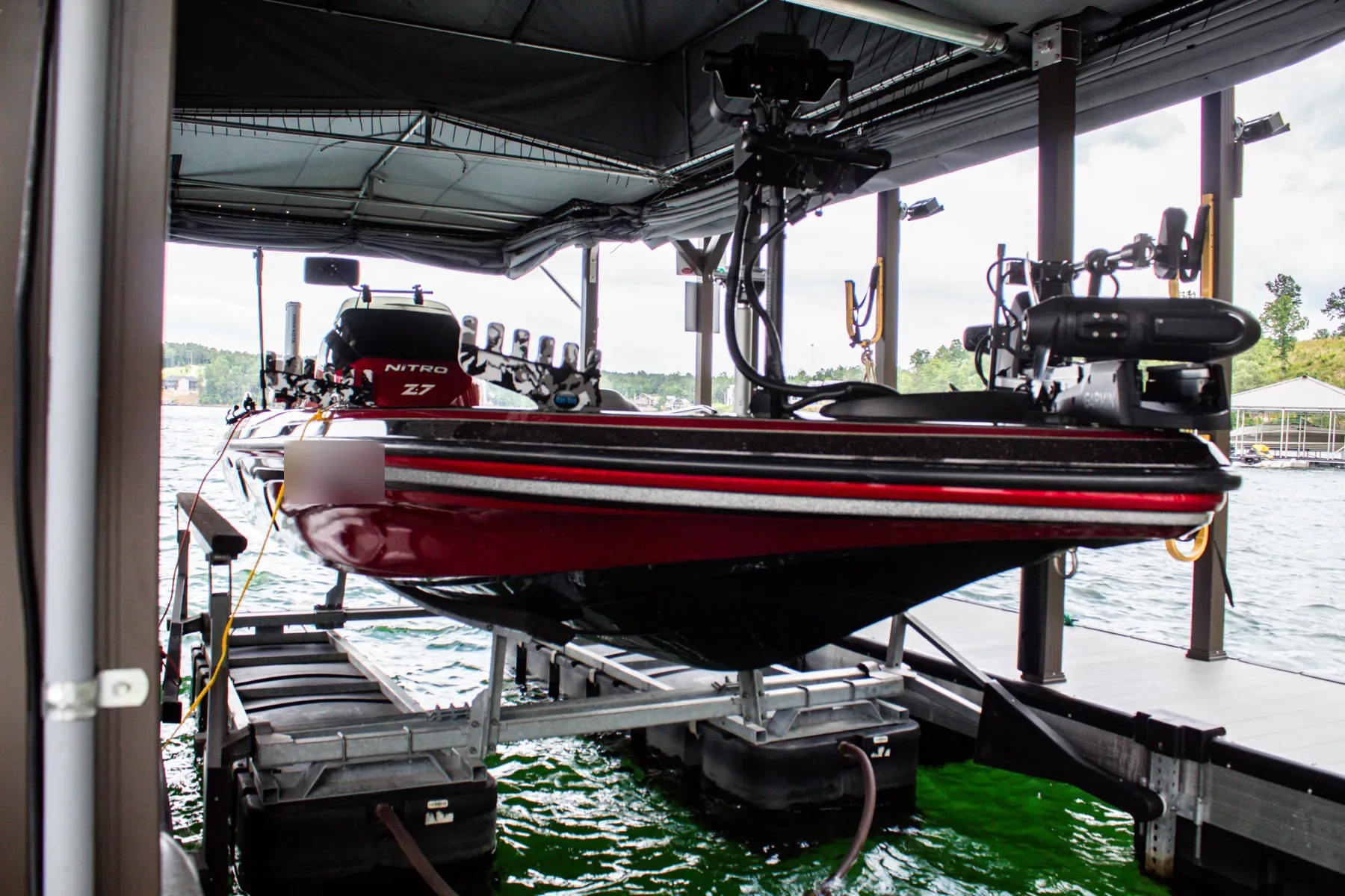 Red and black bass boat on a boat lift with a trolling motor and fish finders